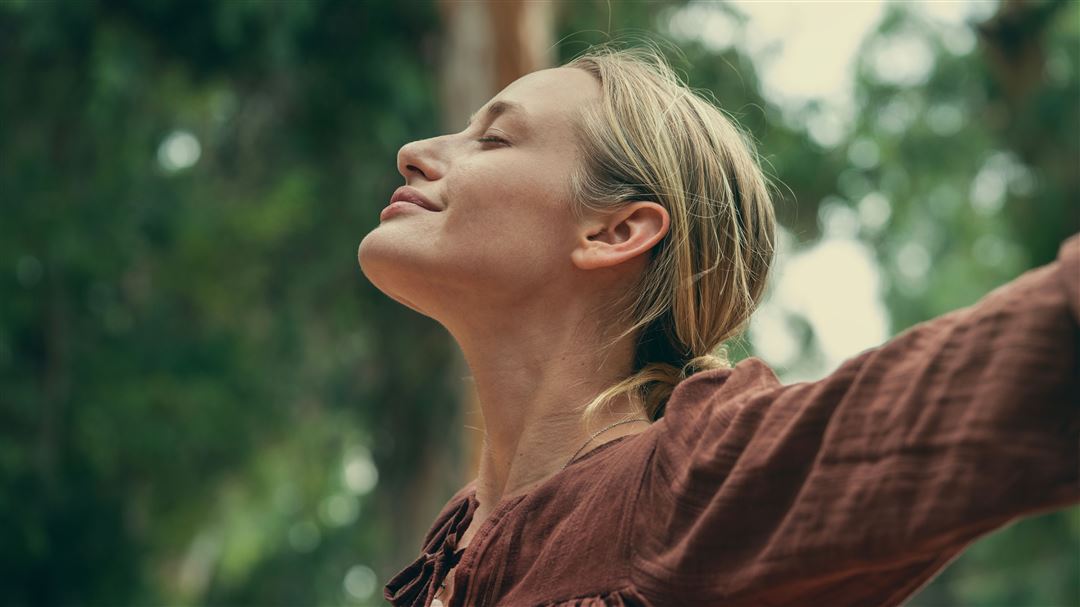Blonde Frau im Wald, l&auml;chelnd, mit ausgestreckten Armen
