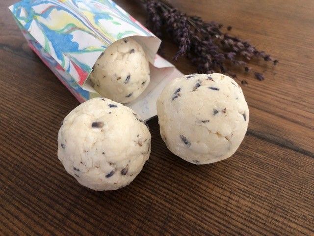 Drei selbstgemachte Seifenb&auml;lle neben einer Papiert&uuml;te auf Holztisch liegend