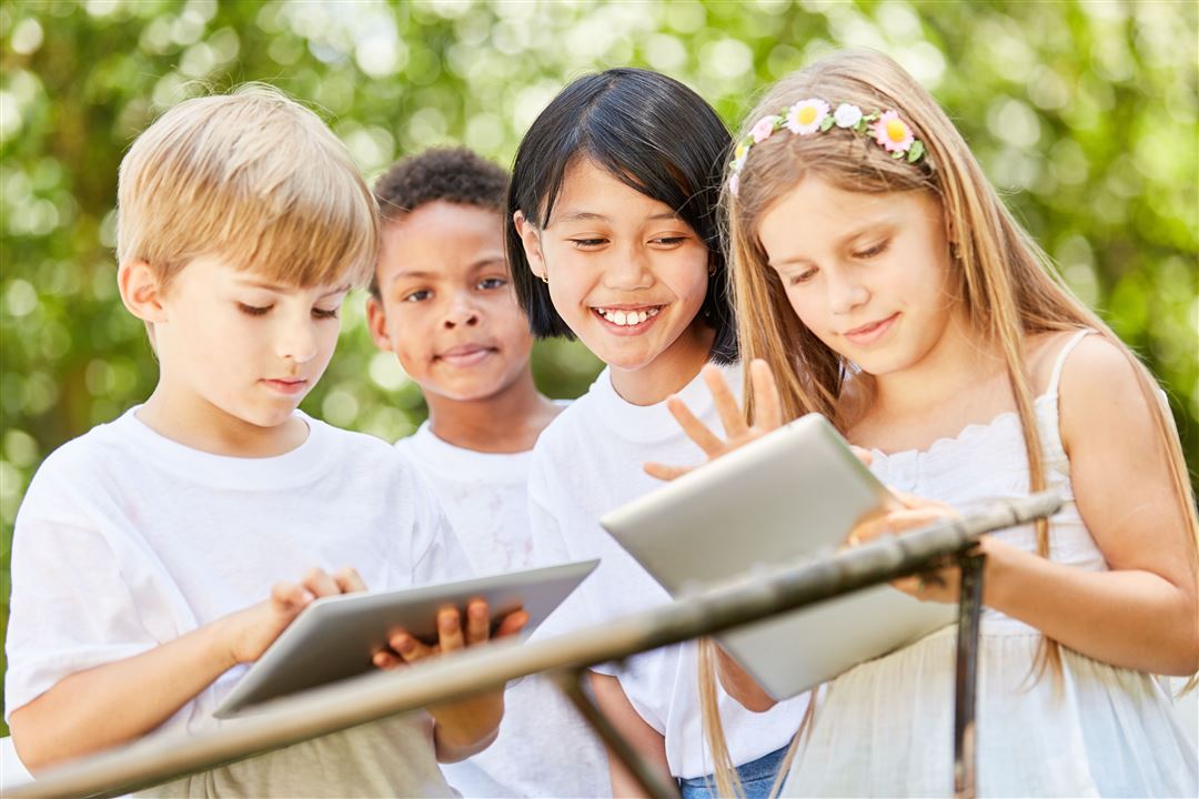 4 Kinder spielen in der Natur mit dem Tablet