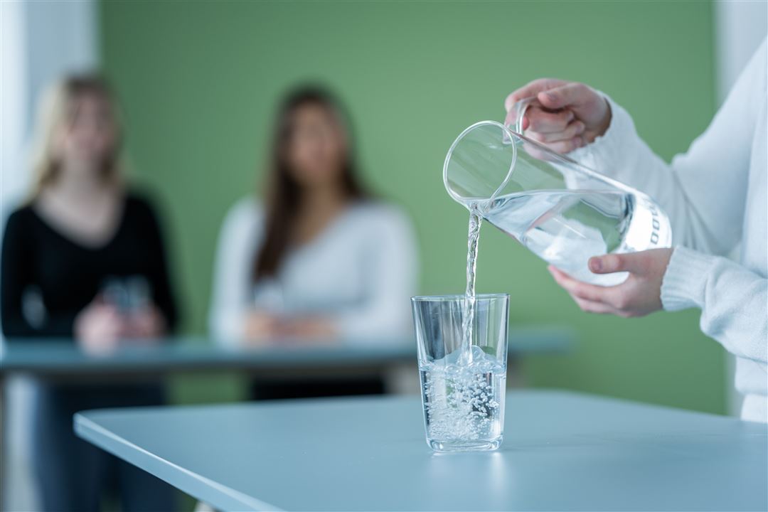 Aus einem Krug wird Wasser in ein Glas eingeschenkt. 