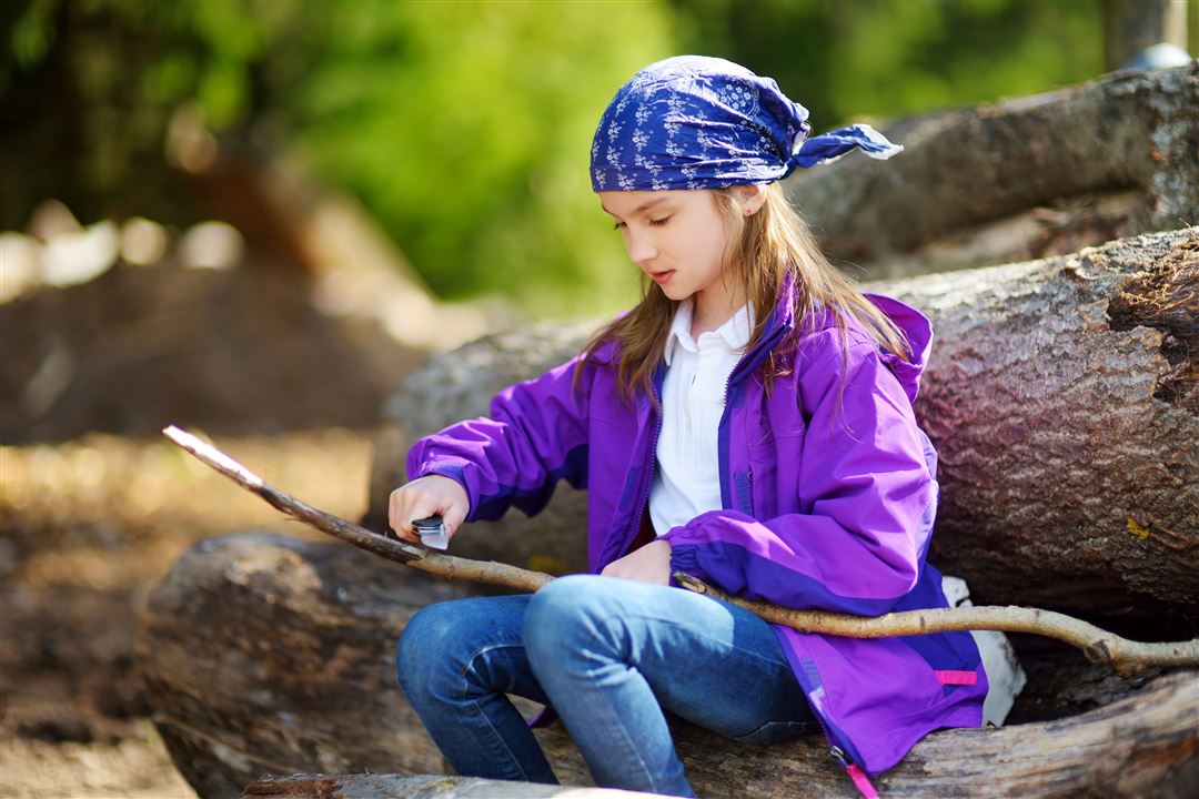 Junges M&auml;dchen sitzt auf Baumstamm und schnitzt Gr&uuml;nholz