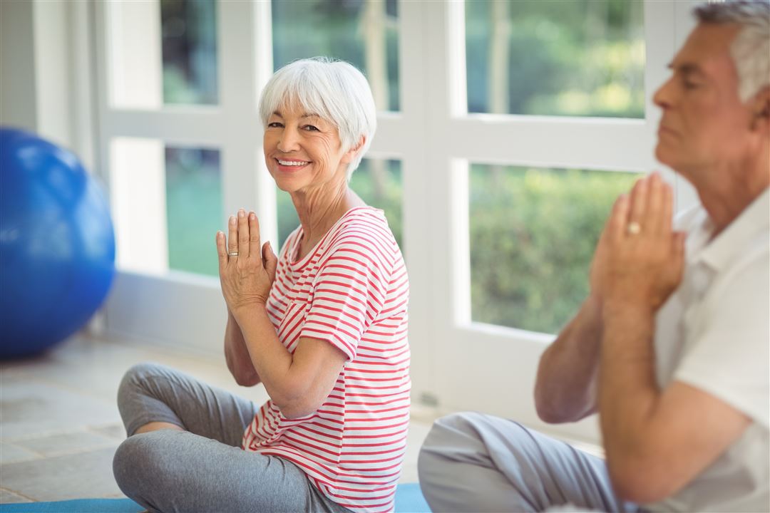 &Auml;ltere Dame praktiziert l&auml;chelnd neben einem Mann eine Yoga-&Uuml;bung