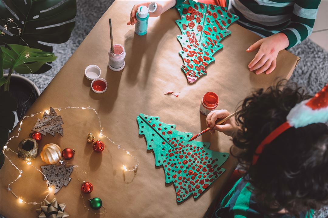 zwei Kinder beim Bemalen eines Tannenbaumes aus Pappe