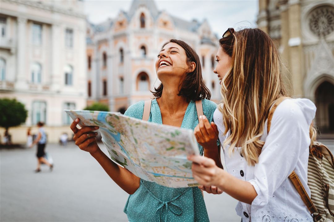 Junge Frauen stehen lachend mit Stadtplan in der Innenstadt
