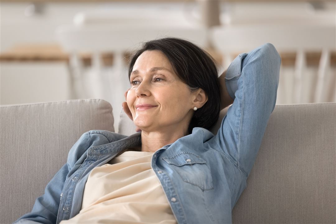 Frau mittleren Alters sitzt l&auml;chelnd und entspannt auf Sofa