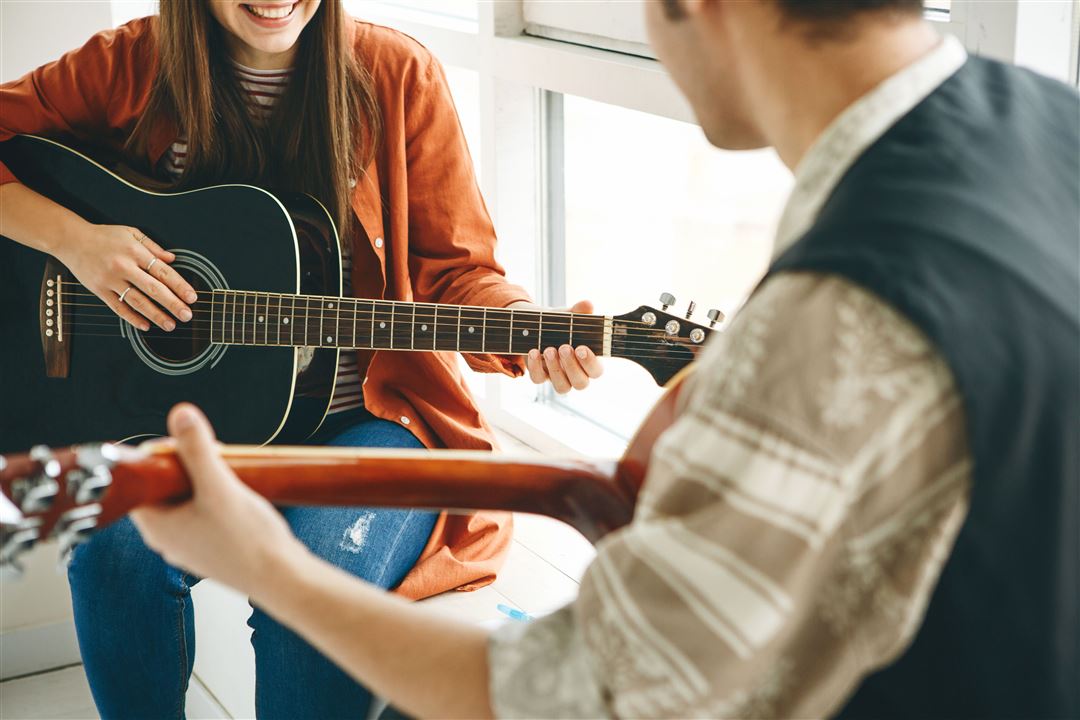 Zwei Personen mit Gitarren in einer Unterrichtssituation.