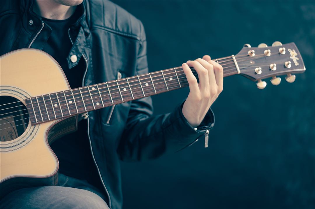 Ein Mann in Lederjacke spielt auf einer Akkustik-Gitarre.